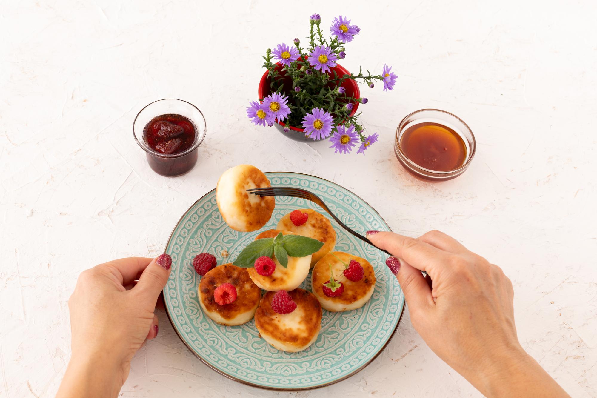Close-up of hands plating a colorful dish on a wooden table